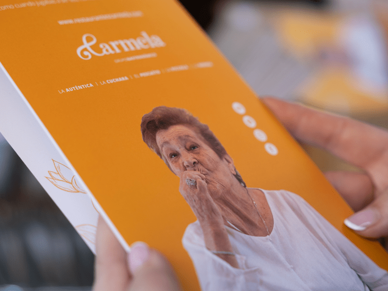 "Carta del restaurante Carmela con diseño naranja mostrando la imagen de una persona mayor en blusa blanca sobre fondo naranja corporativo"