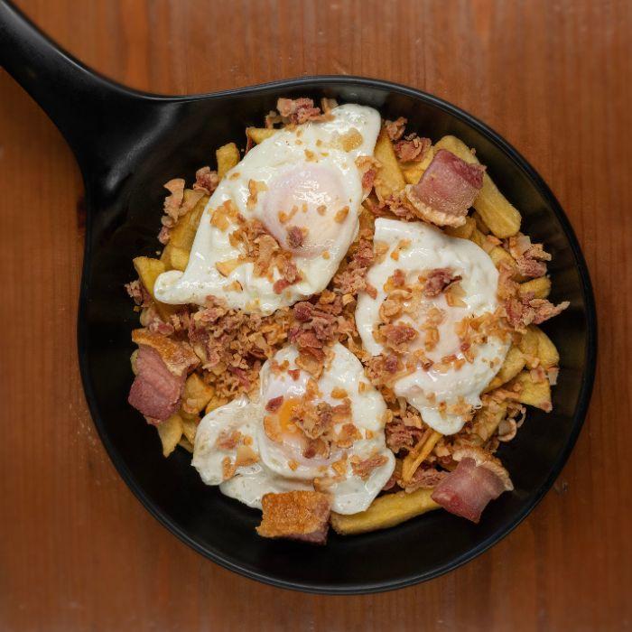 Huevos rotos con torreznos y patatas fritas servidos en sartén en La Auténtica Carmela