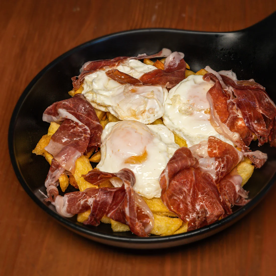 Huevos rotos con jamón ibérico servidos en sartén en La Auténtica Carmela, Granada