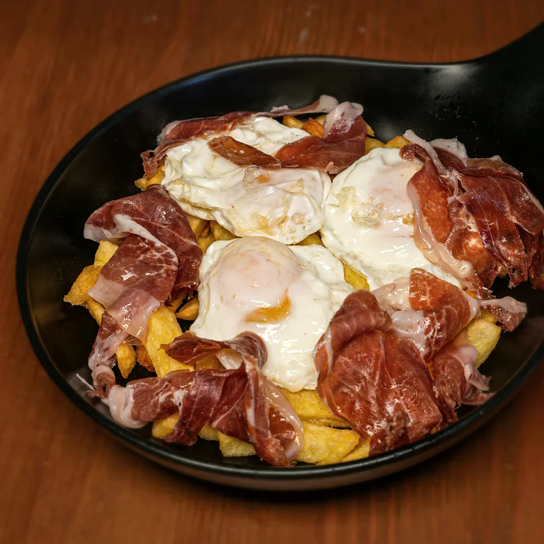 Huevos rotos con jamón ibérico servidos en sartén en La Auténtica Carmela