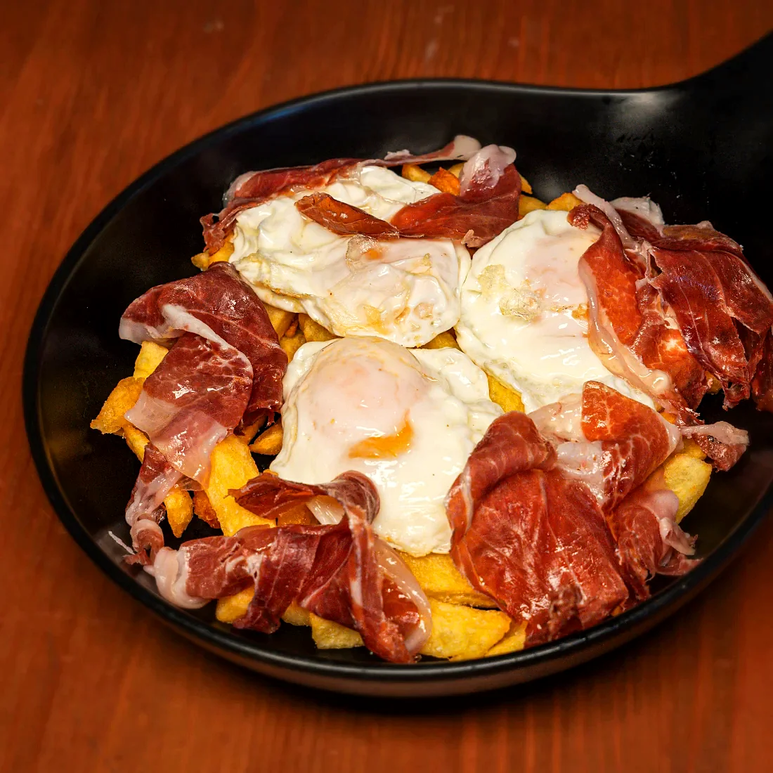 Huevos rotos con jamón ibérico servidos en sartén en La Auténtica Carmela