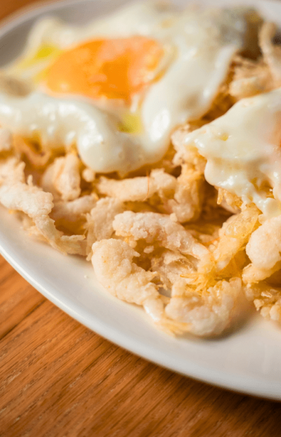 "Primer plano de huevos fritos con yema jugosa sobre base de gambas cristal crujientes en plato blanco"